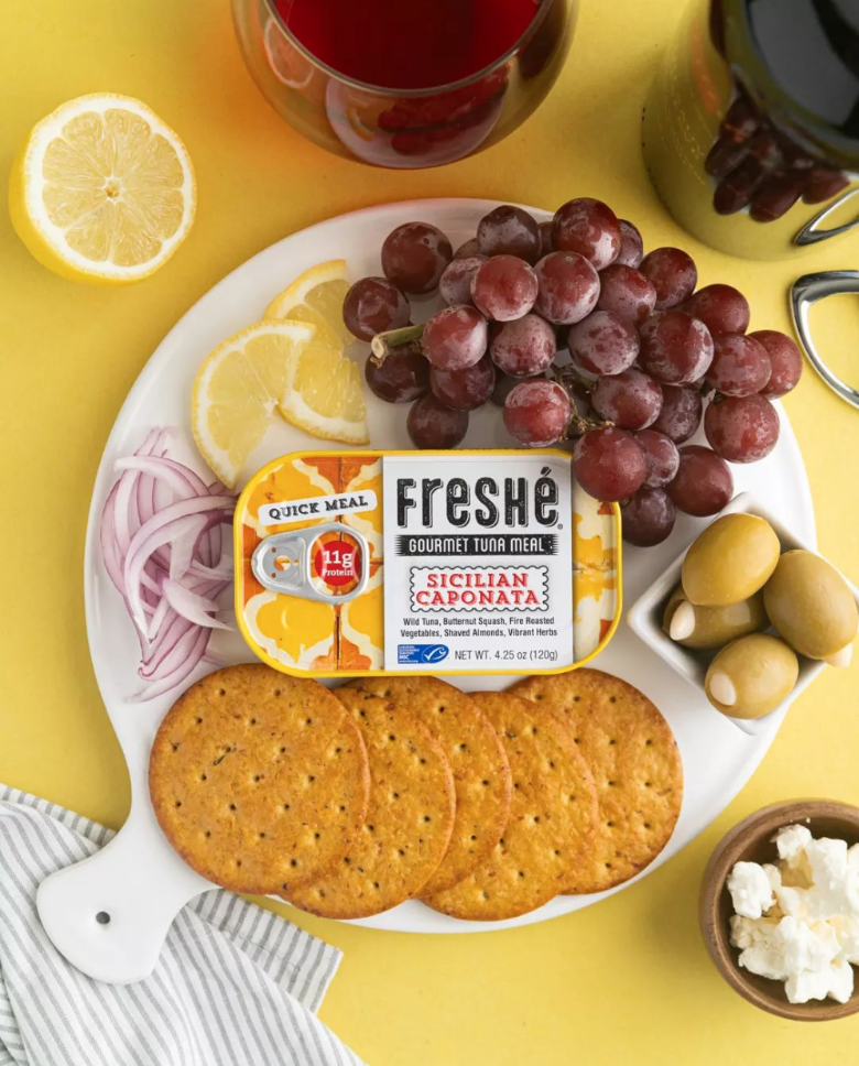 Freshé Sicilian Caponata tuna tin on a snack platter with crackers, grapes, lemon slices and olives